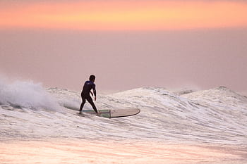 A surfer gracefully rides waves during a stunning summer sunset. HD wallpaper