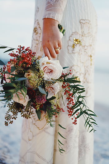 A bride holding a beautiful floral bouquet, showcasing elegance and tradition on her wedding day. HD phone wallpaper