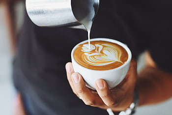 Close-up of a barista pouring milk to create latte art in a coffee cup. HD wallpaper