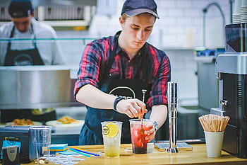 A barista in a casual cafe setting preparing refreshing drinks with focus and skill. HD wallpaper