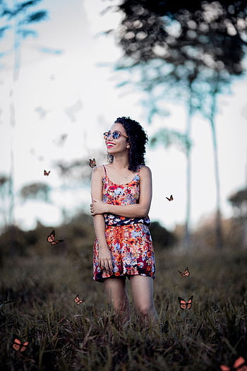 Happy woman in a vibrant dress surrounded by butterflies in a sunny park setting. HD phone wallpaper