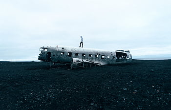 Eerie scene of an abandoned plane wreck on Icelandic beach with a person standing on top. HD wallpaper