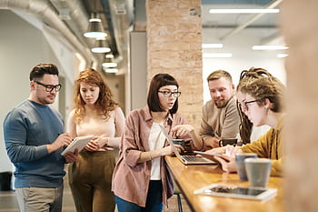 A diverse group of coworkers in a modern office engaged in teamwork using technology. HD wallpaper