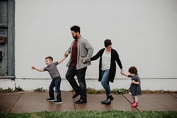 A joyful family walking together outdoors, holding hands in a playful and happy moment. HD wallpaper