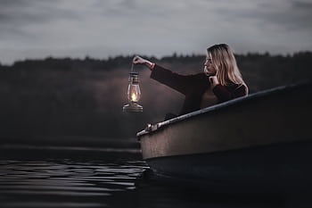 A contemplative woman in a boat holding a lantern during twilight on a calm lake. HD wallpaper