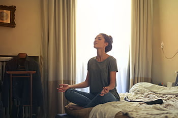 Adult woman practicing meditation on her bed surrounded by a calm bedroom atmosphere. HD wallpaper