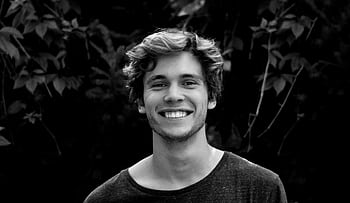 A black and white portrait of a young man smiling outdoors with natural background. HD wallpaper