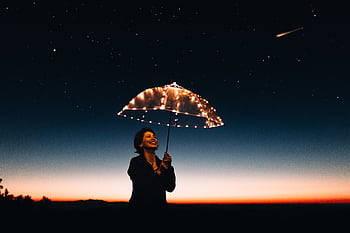 A joyful woman with a light-up umbrella stands under a starry sky, capturing a magical moment. HD wallpaper