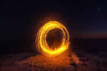 Captivating long exposure shot of a fire dancer creating fiery circles on a serene beach at night. HD wallpaper