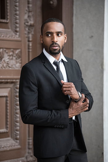 Elegant man in a black suit posing confidently outdoors with a serious expression. HD phone wallpaper