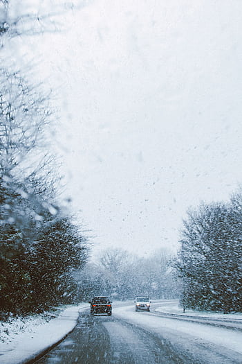 A scenic winter road with cars driving through a snowstorm, surrounded by frosty trees. HD phone wallpaper