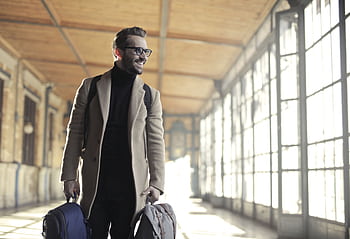 Smiling man in a winter coat with bags walking through a bright train station corridor. HD wallpaper