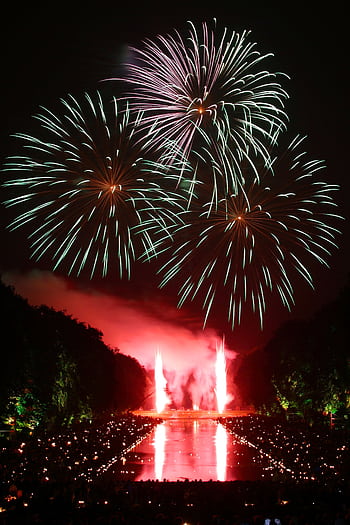 Dazzling fireworks illuminate the night sky with reflections on water, perfect for festive occasions. HD phone wallpaper