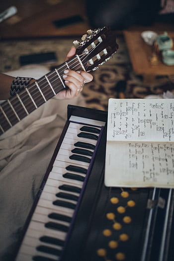 Close-up view of a guitar and keyboard with sheet music, capturing a cozy indoor music session. HD phone wallpaper