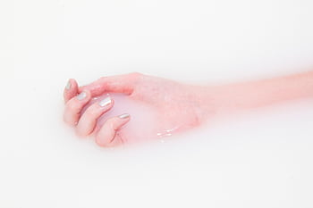 A woman's manicured hand soaks in milky water, creating a minimalist and soothing texture. HD wallpaper