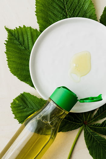 A green cosmetic bottle and oil drop on a plate surrounded by fresh leaves. HD phone wallpaper