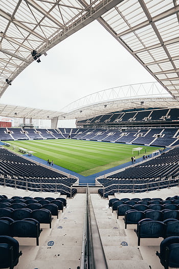 Wide-angle view of a contemporary stadium featuring empty bleachers and a well-maintained grass field, perfect for various sports. HD phone wallpaper