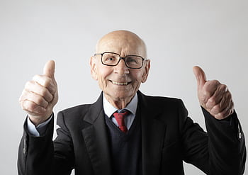 Cheerful elderly man in suit giving thumbs up, symbolizing success and approval. HD wallpaper