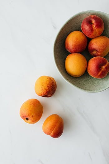 Top view of ripe apricots in a bowl on a marble surface, showcasing their vibrant colors. HD phone wallpaper