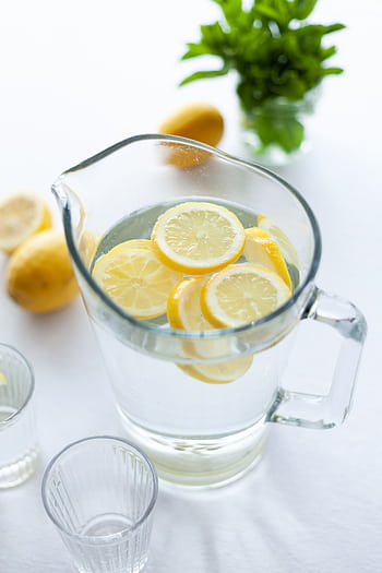 A glass pitcher filled with fresh lemon water, surrounded by lemons and mint, on a bright table. HD phone wallpaper