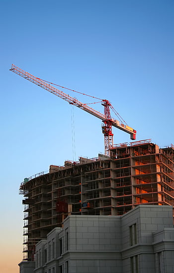 Tower crane on a high-rise building under construction at sunset, showcasing modern urban development. HD phone wallpaper