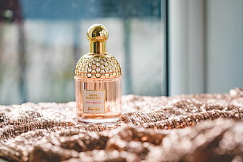 Elegant Guerlain perfume bottle on a textured fabric with natural lighting, exuding luxury and fragrance. HD wallpaper