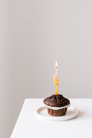 Minimalist of a chocolate cupcake with a lit spiral candle on a white background. HD phone wallpaper
