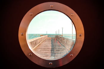 Captivating view of a wooden pier extending into the ocean through a round window. HD wallpaper