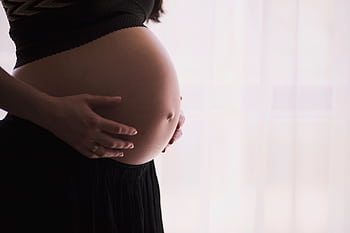 A close-up of a pregnant woman touching her bare belly, expressing warmth and care. HD wallpaper