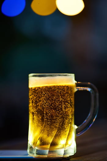 A glass mug of cold beer with frothy head and bokeh lighting effect in a dim setting. HD phone wallpaper