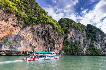 A boat cruise offers breathtaking views of lush cliffs under a bright blue sky. HD wallpaper