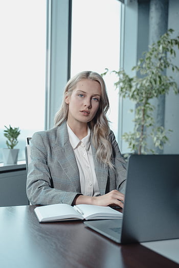 Portrait of a confident businesswoman working on her laptop in a modern office setting. HD phone wallpaper