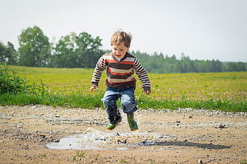 A cheerful child in a striped sweater jumps into a puddle on a sunny day in Czechia. HD wallpaper