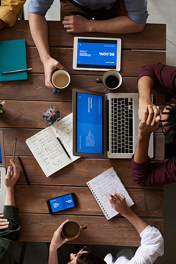 Group of coworkers discussing business strategies with laptops and tablets in a modern office setting. HD phone wallpaper