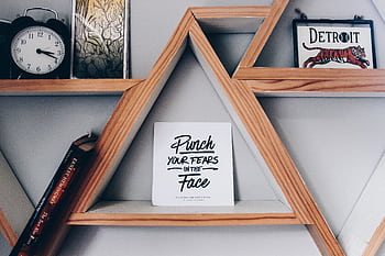 Triangular wooden bookshelf with motivational quote sign, clock, and decor. HD wallpaper