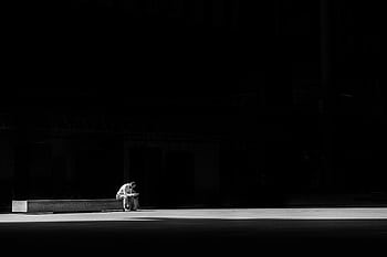 A lone man sitting on a bench, captured in striking black and white, conveying solitude and contemplation. HD wallpaper