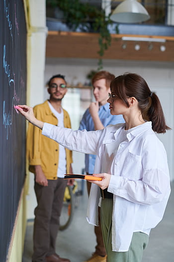 A group of young people discussing ideas at a blackboard in a modern office setting. HD phone wallpaper