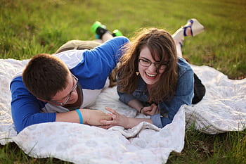 Smiling couple relaxing on a blanket during a sunny day picnic in a grassy field. HD wallpaper