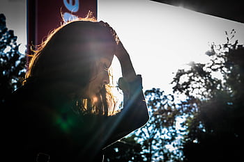 A silhouette of a woman touching her head, surrounded by nature and sunlight. HD wallpaper
