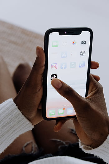 Hands holding a smart showing various apps including TikTok in a close-up view. HD phone wallpaper