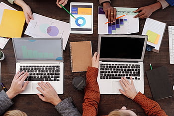 Overhead view of a team discussing digital marketing strategies with laptops and charts. HD wallpaper