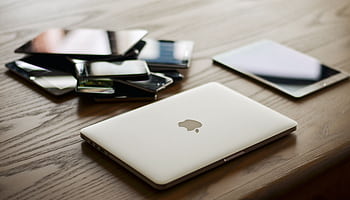 A variety of modern electronic gadgets, including a laptop and smarts, on a wooden table. HD wallpaper