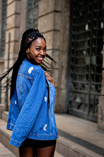 Stylish woman with braided hair smiling outdoors in denim jacket. HD phone wallpaper