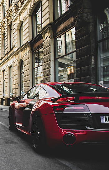 Sleek red sports car parked on a charming historic street in Prague, highlighting urban elegance and powerful design. HD phone wallpaper