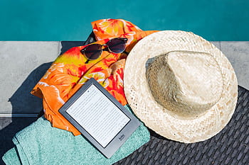 Flat lay of summer essentials by the pool with e-reader, sunhat, and vibrant towel. HD wallpaper