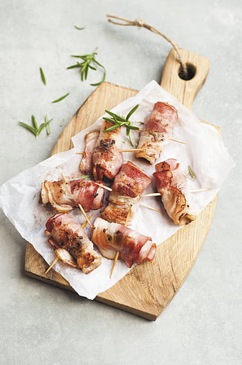 Delicious bacon wrapped chicken bites on a wooden board with herbs, perfect for a savory appetizer. HD phone wallpaper