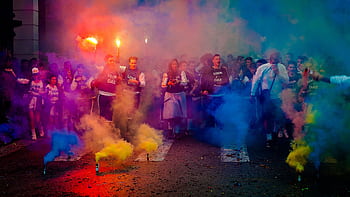 A lively group celebrating at night with color smoke bombs in a street festival. HD wallpaper