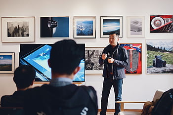 Man giving a presentation in a modern art gallery setting, engaging audience. HD wallpaper