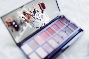 Close-up of makeup brushes in a decorative holder and a colorful eyeshadow palette. HD wallpaper