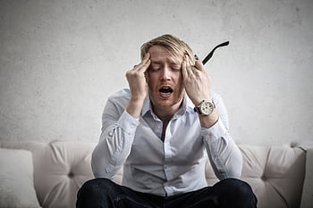 Stressed man sitting on couch, feeling overwhelmed and frustrated, expressing mental strain. HD wallpaper